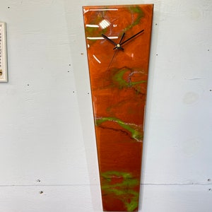 Könnte beinhalten: Eine lange, schmale, orangefarbene und grüne Harz-Uhr mit einem schwarzen Zifferblatt und Zeigern.