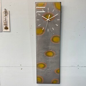 May include: A gray and white clock with yellow and orange accents. The clock is framed in a black frame and has a white face with black hands.