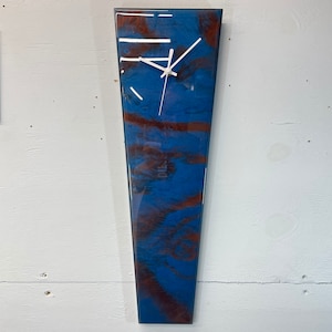 May include: A long, narrow, blue and brown resin clock with white hands. The clock is mounted on a white wall.
