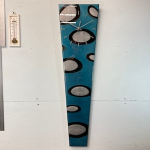 May include: A teal blue clock with a white face and silver hands. The clock has a unique design with white and black circles on the face.