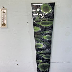 May include: A black and green abstract clock with white hands. The clock is shaped like a long, thin rectangle.