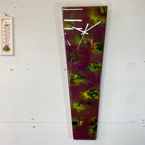 May include: A long, narrow, abstract clock with a white face and black hands. The clock face is set against a background of purple and green resin.