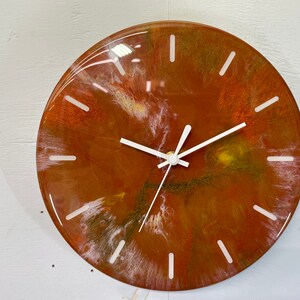 May include: A round, brown, white and gold resin clock with white hands. The clock face has a swirling, abstract design.