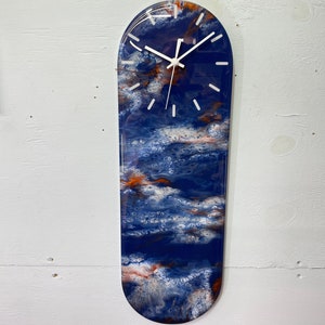 May include: A blue and orange abstract resin clock with white clock hands. The clock is shaped like a skateboard.