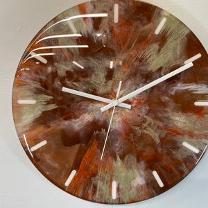 May include: A round clock with a white face and white hands. The clock face has a brown, orange, and white abstract design.