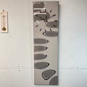 May include: A grey and white abstract clock with black hands. The clock face is made of resin and has a unique design with grey and white circles.