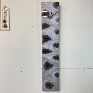 May include: A white and black abstract clock with a black clock face and black hands. The clock is mounted on a white wall.