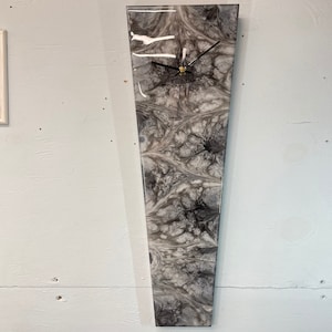 May include: A grey and white abstract clock with black hands. The clock is shaped like a long, thin triangle.