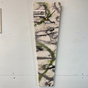 May include: A white, black, and green abstract art clock with black hands. The clock is mounted on a white wall.