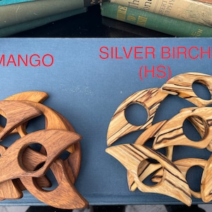 Op de afbeelding: Twee sets houten onderzetters, &eacute;&eacute;n set is gemaakt van mango hout en de andere van zilverberk hout. De mango houten onderzetters zijn een rijke bruine kleur en de zilverberk houten onderzetters hebben een lichtbruine kleur met donkerbruine strepen. De onderzetters zijn gevormd als een halve maan.