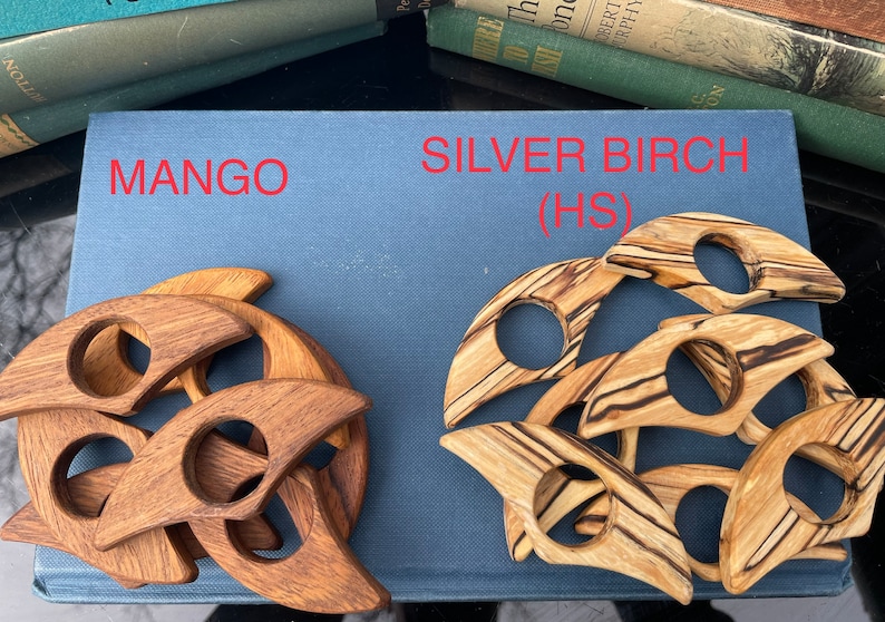 Op de afbeelding: Twee sets houten onderzetters, &eacute;&eacute;n set is gemaakt van mango hout en de andere van zilverberk hout. De mango houten onderzetters zijn een rijke bruine kleur en de zilverberk houten onderzetters hebben een lichtbruine kleur met donkerbruine strepen. De onderzetters zijn gevormd als een halve maan.