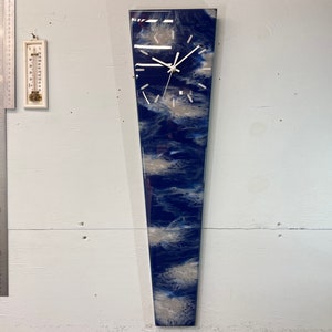May include: A long, narrow, blue and white resin clock with a white face and black hands. The clock is mounted on a white wall.