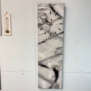Può includere: Un orologio in resina bianco e grigio con lancette nere. Il quadrante dell'orologio ha uno sfondo bianco con segni neri per le ore e i minuti. L'orologio è montato su una parete bianca.