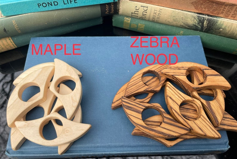 Op de afbeelding: Twee sets houten boekenleggers, een set gemaakt van esdoornhout en de andere van zebrahout. Beide sets hebben de vorm van een halve maan.