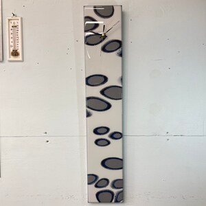 May include: A long, rectangular clock with a white background and a pattern of gray and blue ovals. The clock has a silver face and black hands.