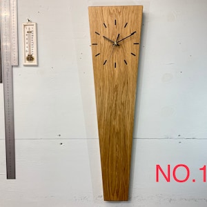 Puede incluir: Un reloj de madera con una esfera y agujas negras. El reloj está montado en una pared y tiene una forma larga y estrecha. El reloj está etiquetado como "NO. 1".