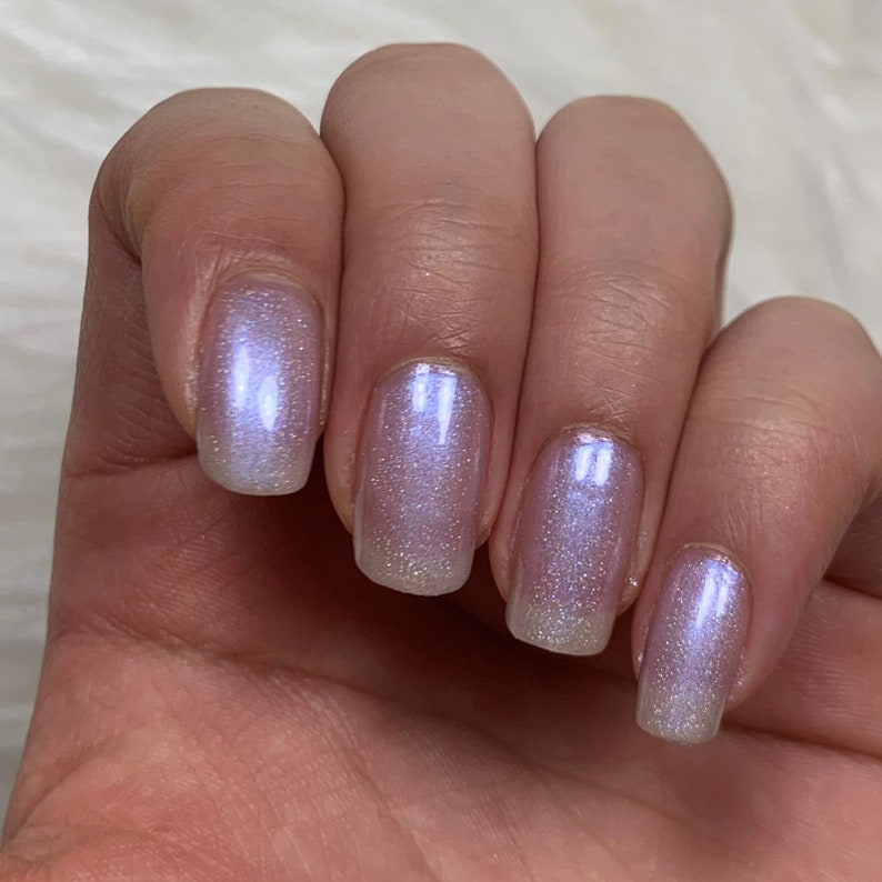May include: Close-up of five fingernails with a light purple iridescent nail polish. The polish has a subtle shimmer and sparkle.