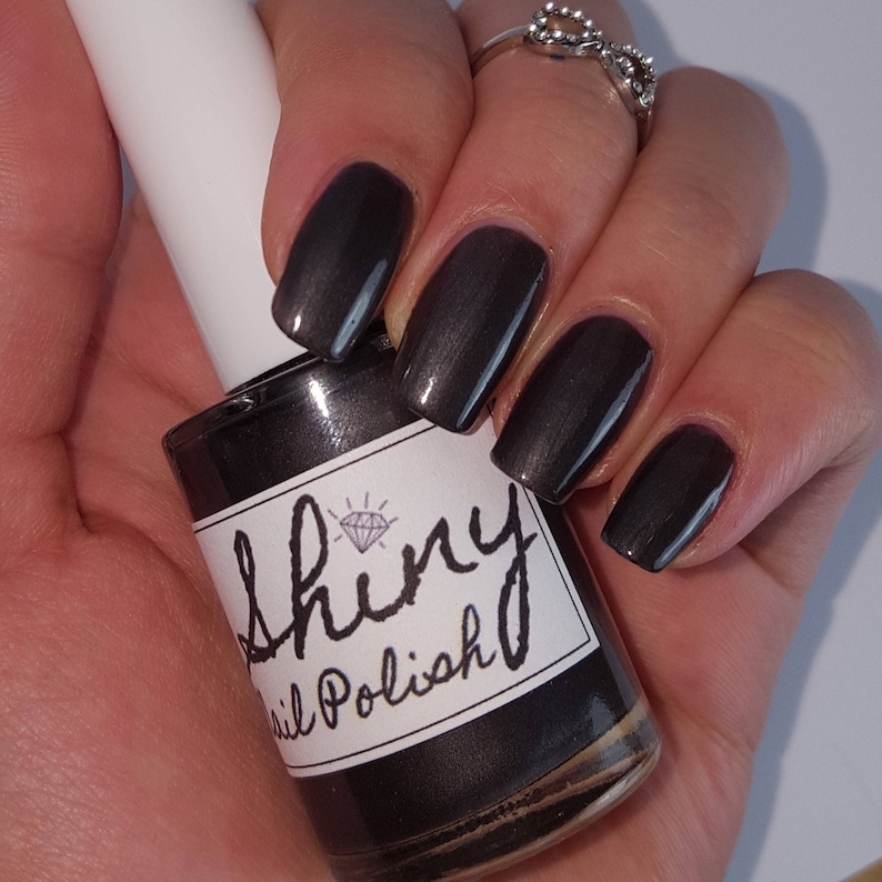 May include: A bottle of dark gray nail polish with a silver shimmer. The bottle has a white label with the text "Shiny Nail Polish" and a diamond logo.