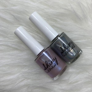 May include: Two bottles of nail polish, one is a light purple with a shimmer and the other is a silver with a shimmer. Both bottles have the text "Shiny Nail Polish" on the label.