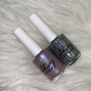 May include: Two bottles of nail polish with a shimmery finish. The bottles are labeled "Shiny Nail Polish" and are in shades of purple and blue.