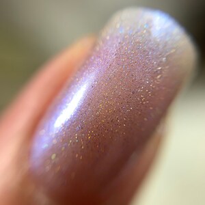 May include: Close-up of a fingernail with a light pink nail polish with iridescent glitter.