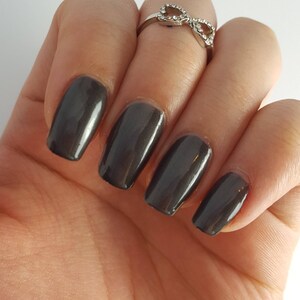 May include: Close-up of a hand with five fingernails painted a dark, metallic gray nail polish.