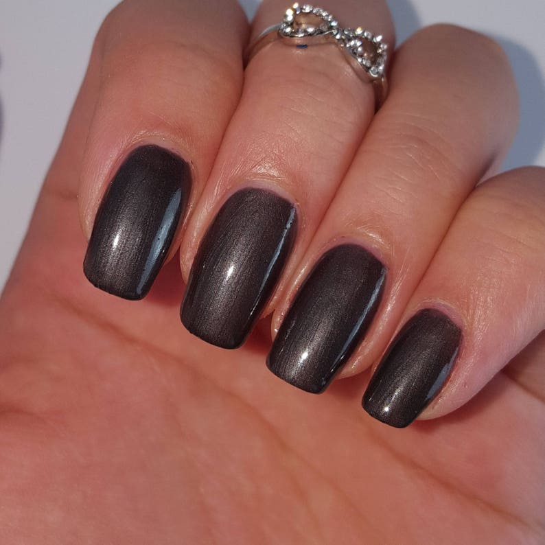 May include: Close-up of a hand with five fingernails painted with a dark, metallic gray nail polish.