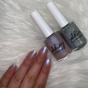 May include: Two bottles of iridescent nail polish with the brand name "Shiny Nail Polish" on the label. The polish is a light purple and a light blue.