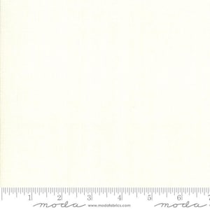 May include: A white fabric with a subtle texture. The fabric is measured in inches with a ruler at the bottom of the image. The ruler has the word "moda" printed on it.