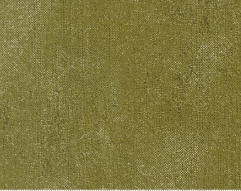 Könnte beinhalten: Ein Stück olivgrüner Stoff mit einer gesprenkelten, strukturierten Optik und einem dezenten Kreuzschraffurmuster. Ein weißes Maßband ist am unteren Rand sichtbar und zeigt Maße in cm bis zu 18 cm, mit dem Text moda und moda fabrics.