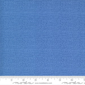 May include: A close-up of a blue textured fabric with a subtle grid pattern. The fabric is measured with a ruler that reads "moda" and includes the website address "www.modafabrics.com".