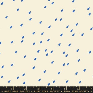 May include: A cream-colored fabric featuring a repeating pattern of small, scattered blue raindrops. At the bottom, a black ruler with white markings and the text "RUBY STAR SOCIETY" spans from 1 to 7 inches, indicating the scale of the print.