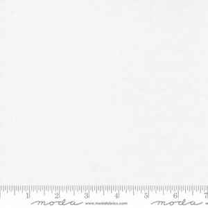 May include: White fabric with a subtle texture. The fabric is measured with a ruler that has the word "moda" printed on it.