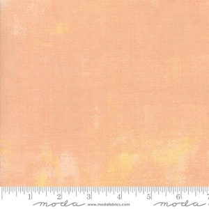 May include: A peach-colored fabric with a subtle, textured pattern. The fabric has a slightly faded, vintage look with hints of yellow throughout.