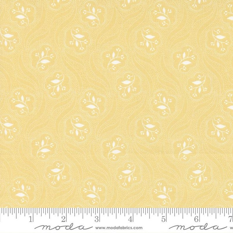 K&ouml;nnte beinhalten: Gelber Stoff mit einem wei&szlig;en, sich wiederholenden Muster aus kleinen Bl&auml;ttern und Punkten. Der Stoff hat ein Lineal mit den Worten "moda" und "www.modafabrics.com" darauf gedruckt.