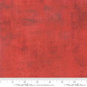 May include: Red fabric with a textured, distressed look. The fabric has a subtle, mottled appearance with a slightly darker red hue in some areas. The fabric is shown with a ruler that reads "moda" and includes a website address.