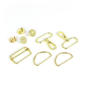 May include: A set of gold-toned metal hardware for bags and purses. The set includes two D-rings, a swivel hook, a rectangle buckle, two snap fasteners, and a lobster clasp.