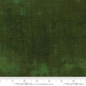 May include: A close-up of a dark green fabric with a textured, slightly distressed look. The fabric has a subtle sheen and a slightly uneven surface. The fabric is measured in inches with a ruler that says "moda" at the 2-inch mark and the 6-inch mark.