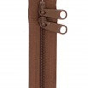 May include: A brown zipper with two sliders. The zipper teeth are a matching brown color. The zipper is shown against a white background.