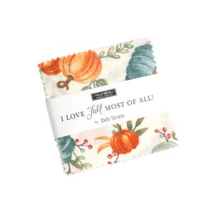 May include: A stack of fabric squares with a fall-themed print featuring pumpkins and foliage. The fabric is wrapped with a white band that reads "I LOVE Fall MOST OF ALL!" by Deb Strain.
