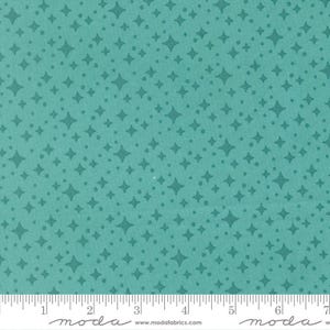 May include: A teal fabric featuring a repeating pattern of dark teal four-pointed stars and small dots. A white ruler is visible at the bottom edge, showing a measurement scale in inches, with the text moda and www.modafabrics.com printed.