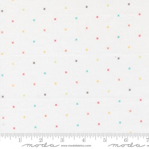 May include: White fabric with a repeating pattern of small, colorful crosses in shades of red, teal, yellow, and gray. The fabric has a ruler along the bottom edge, with the word "moda" printed on it.