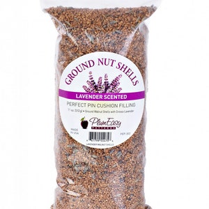 May include: A clear plastic bag filled with ground walnut shells, lavender scented, for pin cushion filling. The bag has a label with the text "Ground Nut Shells" and "Lavender Scented". The bag contains 11 oz. (312g) of ground walnut shells with Grosso Lavender.
