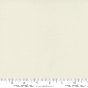 May include: A close-up of a plain, off-white fabric with a subtle texture. The fabric is measured with a ruler in inches, with the text "moda" printed on the ruler.