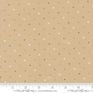 May include: A tan fabric featuring a repeating pattern of small, evenly spaced white and olive green polka dots. A white ruler is visible at the bottom edge, showing measurements in inches from 0 to 7, with the text moda and modafabrics.com.