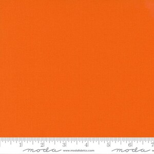 May include: Solid orange fabric swatch with a subtle texture. The fabric is measured in inches with the text "moda" printed on the ruler.