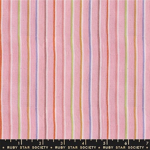 May include: Pink fabric with vertical stripes in various colors, including orange, white, green, blue, and brown. The fabric has a textured appearance and is suitable for sewing projects. The bottom of the image has the text "RUBY STAR SOCIETY".