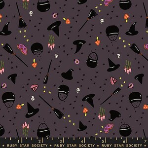 May include: A dark gray fabric featuring a repeating pattern of black witch hats, black cauldrons, black broomsticks, white skulls, orange mushrooms, pink flowers, and purple butterflies, with yellow stars and a ruler showing 7 inches.