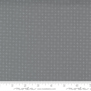 May include: A grey fabric featuring a repeating pattern of small white plus signs and dots arranged in a grid. A white ruler is visible at the bottom edge, showing measurements in inches, with the text moda and www.modafabrics.com printed.
