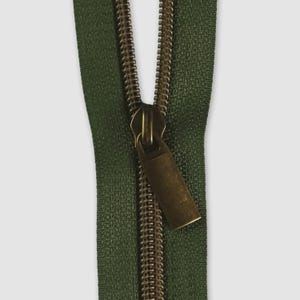 May include: A forest green zipper featuring a metallic bronze-toned slider and a rectangular pull tab. The zipper teeth are also finished in a matching bronze tone, contrasting against the dark green fabric tape of the fastener mechanism.